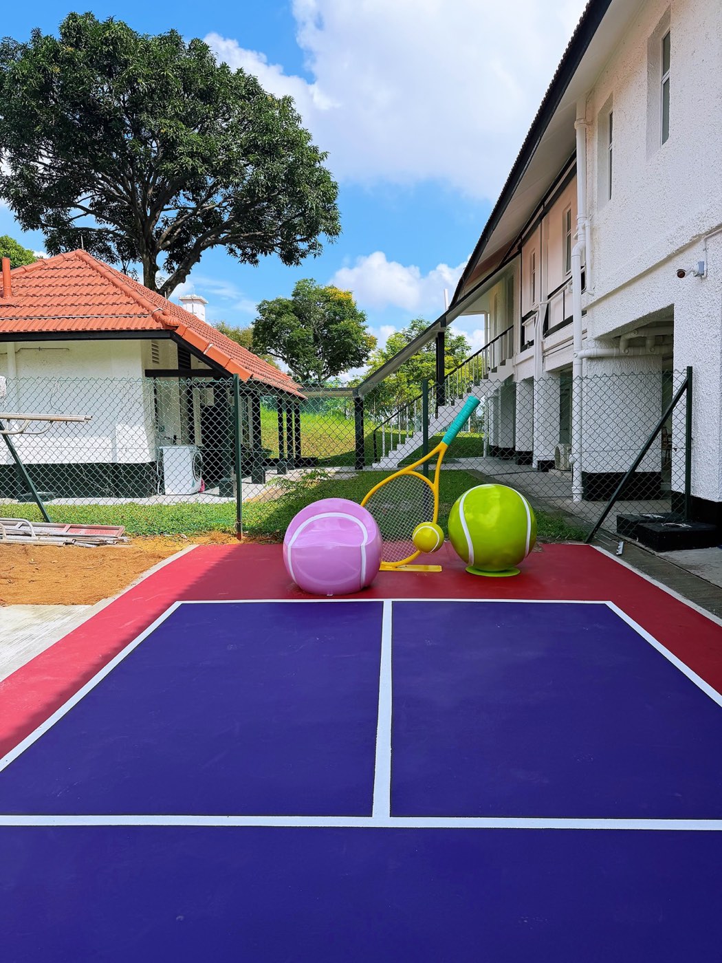 A small purple hard court with a red surround and oversized decorative tennis balls and racket at the far end.